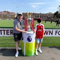 A man and a boy standing either side of a plinth with the Premier League trophy with red-and-white ribbons.